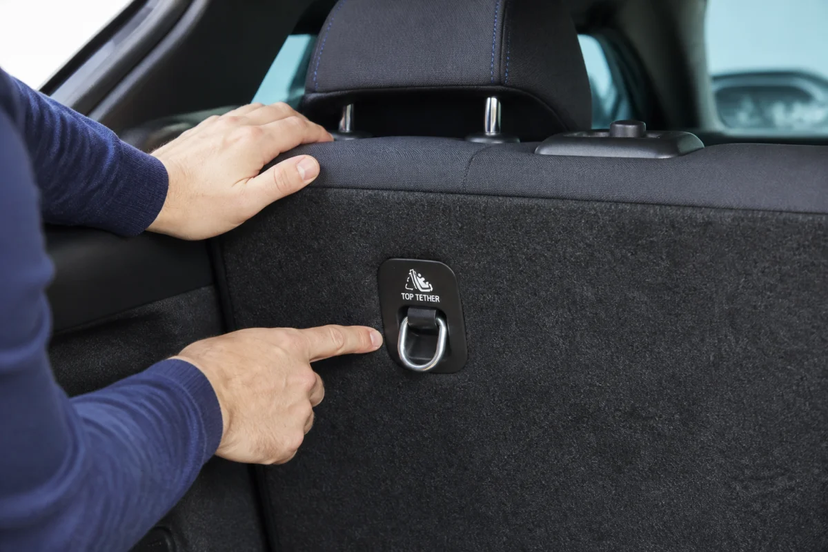 Gros plan sur une main inspectant l'anneau métallique d'ancrage Isofix pour savoir si la voiture est compatible.